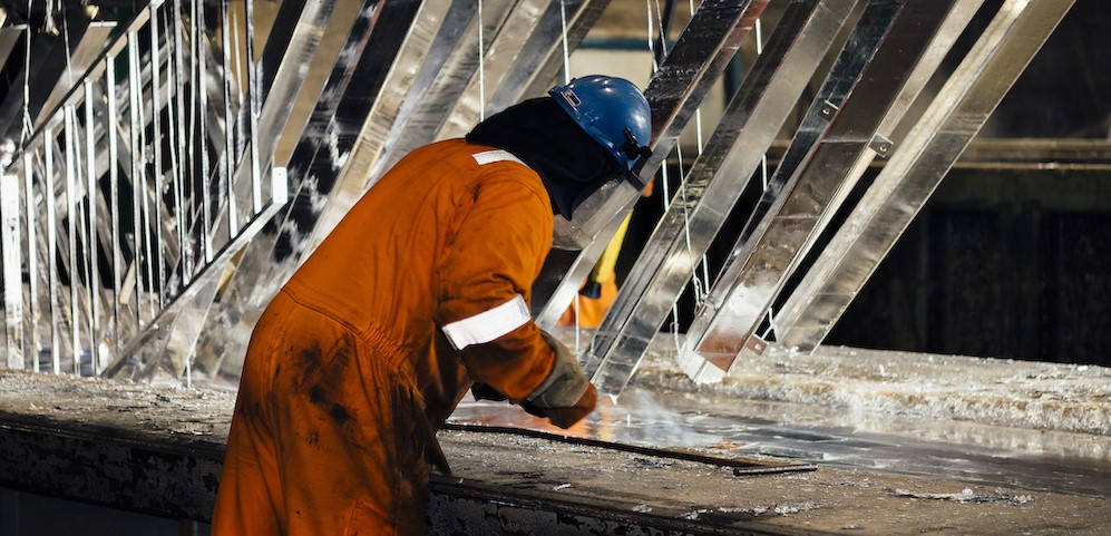 A man in orange safety gear hot dip galvanizing steel beams